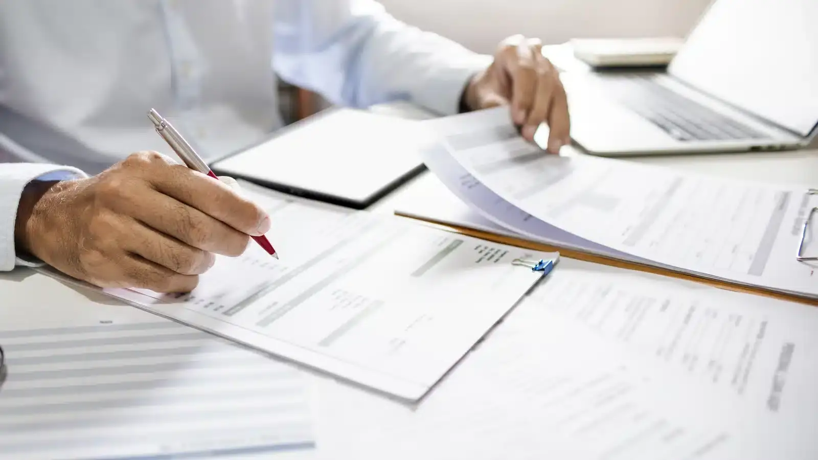 Hands reviewing printed documents beside a laptop, illustrating the pre-publish compliance check every piece of aesthetic marketing should pass.
