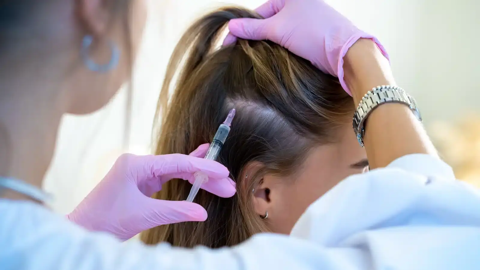 A clinician's gloved hands administering a scalp treatment at an aesthetic practice, illustrating how patient reviews often follow the individual injector rather than the clinic.